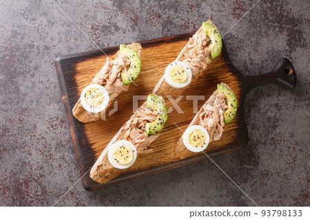 Healthy diet sandwiches with canned tuna, boiled egg, ripe avocado and sesame close-up on a wooden board. Horizontal top view Healthy diet sandwiches with canned tuna, boiled egg, ripe avocado and sesame close-up on a wooden board. Horizontal top view 93798133