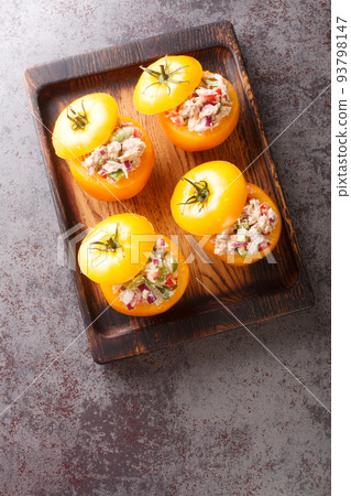 Fresh yellow tomatoes stuffed with tuna salad and vegetables close-up on a wooden tray. Vertical top view Fresh yellow tomatoes stuffed with tuna salad and vegetables close-up on a wooden tray. Vertical top view 93798147