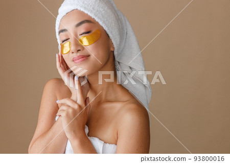 Smiling Asian woman using under-eye patches after shower 93800016