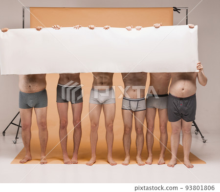 Group of body positive men standing together in underwear. Models holding big blank paper banner closing faces. Body positive concept 93801806