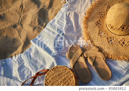 Top view of beach accessories. Straw hat, bag, flip flops on sand at beach. 93803912