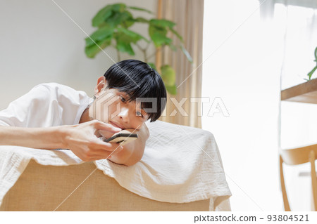 A man looking at a smartphone while lazing on the sofa 93804521