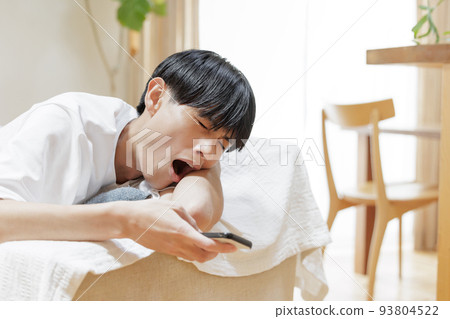 A man looking at a smartphone while lazing on the sofa 93804522