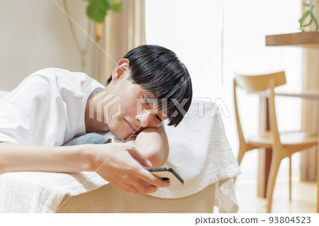 A man looking at a smartphone while lazing on the sofa 93804523