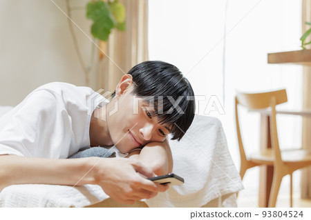 一個男人懶洋洋地躺在沙發上看智能手機 93804524