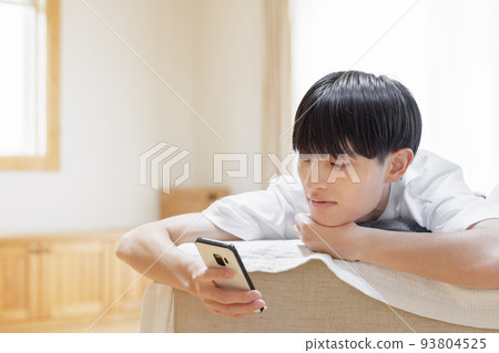 A man looking at a smartphone while lazing on the sofa 93804525