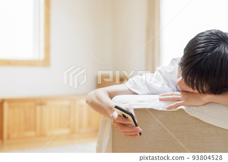 A man looking at a smartphone while lazing on the sofa 93804528