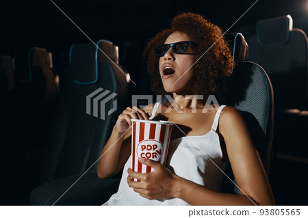 A young woman in 3D glasses is watching a movie enthusiastically. Popcorn in hands. 93805565