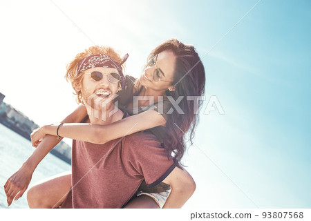 Outdoors photo of happy boyfriends piggybacking their girlfriends at sunset on beach 93807568