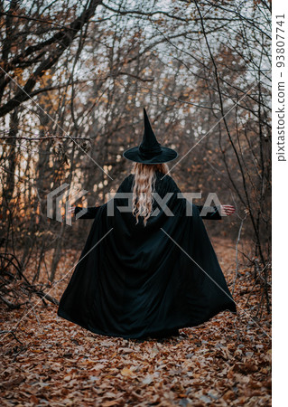 Blonde witch in long black cape and hat on autumn forest background. Spooky horror halloween, wizard 93807741