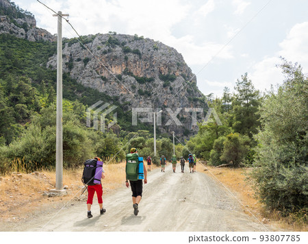 Tourists with backpacks walk to Goynuk Canyon. Path along mountain slopes in Beydaglari Coastal National Park. Turkey. 93807785