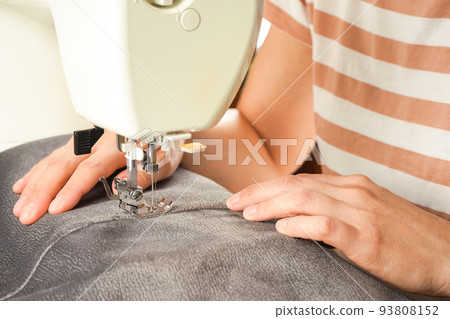 Female hands stitching gray fabric on modern sewing machine. Close up view of sewing process. Female hands stitching gray fabric on modern sewing machine. Close up view of sewing process. 93808152
