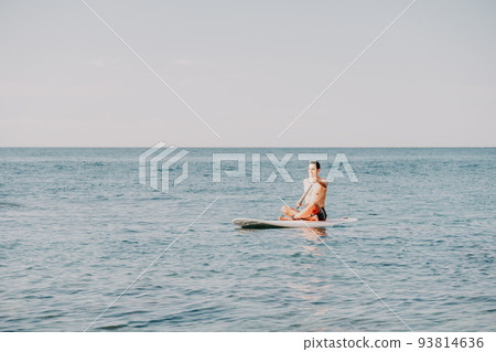 Side view foto of a man swiming and relaxing on the sup board. Sportive man in the sea on the Stand Up Paddle Board SUP. The concept of an active and healthy life in harmony with nature. 93814636