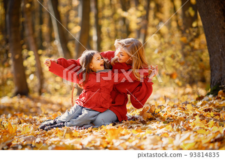 Young woman with little girl sitting on a blanket in autumn forest. Blonde woman play with her daughter. Mother and daughter wearing jeans and red jackets. Young woman with little girl sitting on a blanket in autumn forest. Blonde woman play with her daughter. Mother and daughter wearing jeans and red jackets. 93814835
