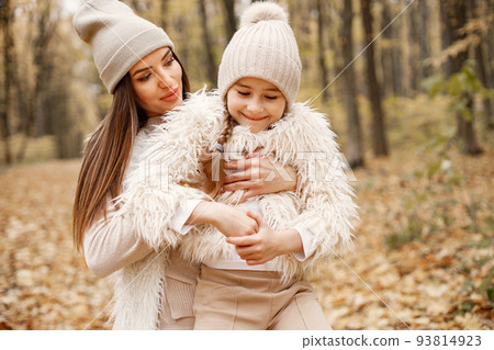 Young woman with little girl standing in autumn forest. Brunette woman play with her daughter. Girl wearing beige sweater and mother wearing white clothes. 93814923