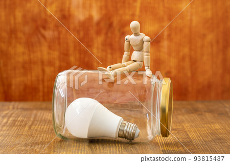 Wooden mannequin sitting on the glass jar with a lightbulb inside 93815487