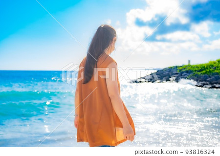 一個女人在夏日閃亮的大海和沙灘上玩耍的背影 93816324