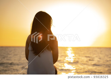 一個女人看著地平線上的日落的後視圖 93816325