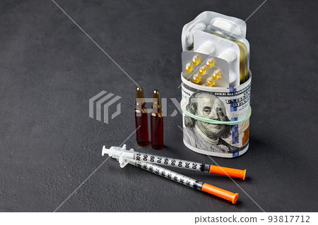 Tablets and ampoules are wrapped in hundred dollar bills, fastened with a rubber band and insulin syringes on a black concrete background Tablets and ampoules are wrapped in hundred dollar bills, fastened with a rubber band and insulin syringes on a black concrete background 93817712