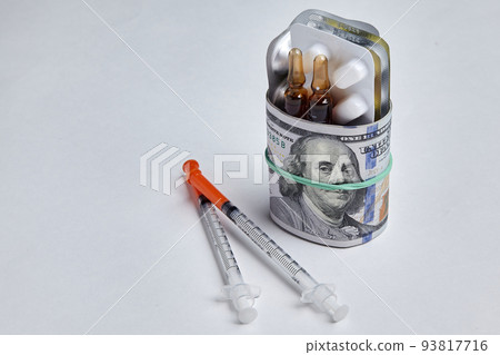 Tablets and ampoules are wrapped in hundred dollar bills, fastened with a rubber band and insulin syringes isolated on a white concrete background Tablets and ampoules are wrapped in hundred dollar bills, fastened with a rubber band and insulin syringes isolated on a white concrete background 93817716