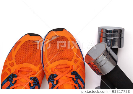 A metal heavy dumbbell fell on a leg in orange torn sneakers on a white background A metal heavy dumbbell fell on a leg in orange torn sneakers on a white background 93817728