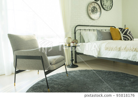 Modern grey armchair next to bed with grey pillows in bedroom interior with large clock on wall. Modern grey armchair next to bed with grey pillows in bedroom interior with large clock on wall. 93818176