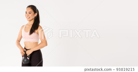 Sport, wellbeing and active lifestyle concept. Smiling strong and slim asian fitness coach, workout trainer or girl in gym lifting kettlebell, do squats with weight, standing white background 93819215