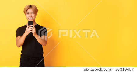 Stylish handsome asian guy taking picture on smartphone and smiling, photographing with mobile phone, standing yellow background Stylish handsome asian guy taking picture on smartphone and smiling, photographing with mobile phone, standing yellow background 93819497
