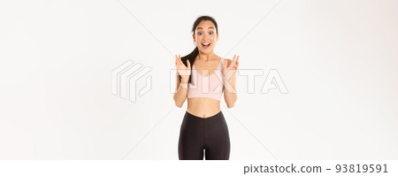 Sport, wellbeing and active lifestyle concept. Happy enthusiastic fitness girl, asian sportswoman clasp hands from fantastic news, gasping amazed, standing over white background 93819591
