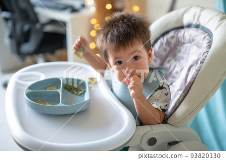 Baby boy eating by himself in his high chair at home 93820130