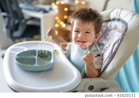 Baby boy eating by himself in his high chair at home Baby boy eating by himself in his high chair at home 93820131