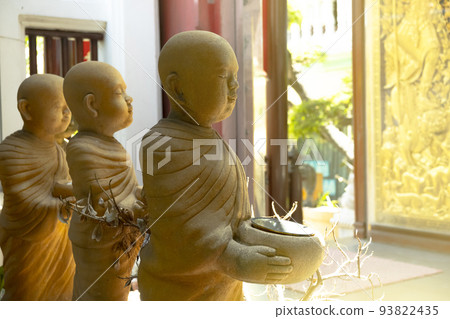 The statue of three monk novice carrying alms bowls decorated in a park at Thai temple and bright background. 93822435