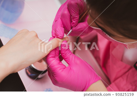 Manicure salon master drawing varnish on the nail tip with a thin brush. Professional manicure in Manicure salon master drawing varnish on the nail tip with a thin brush. Professional manicure in 93825159