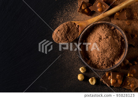Broken chocolate nuts pieces and cocoa powder on dark background Broken chocolate nuts pieces and cocoa powder on dark background 93828123