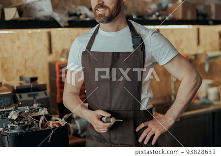 Unrecognizable repairman with a screwdriver standing on own workshop with coffee machines 93828631