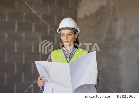 woman engineer in a white helmet and a protective vest holds a model house construction plan in her hands. construction sale and purchase woman engineer in a white helmet and a protective vest holds a model house construction plan in her hands. construction sale and purchase 93829905