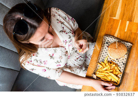 Burger eating pregnant woman. Pretty young pregnancy girl eat tasty hamburger. Junk food concept. Burger eating pregnant woman. Pretty young pregnancy girl eat tasty hamburger. Junk food concept. 93832637
