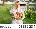 Young woman in white dress sitting on the grass with basket with assorti of brown and white homemade bread. High quality photo 93833235