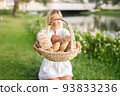 Young woman in white dress sitting on the grass with basket with assorti of brown and white homemade bread. High quality photo 93833236