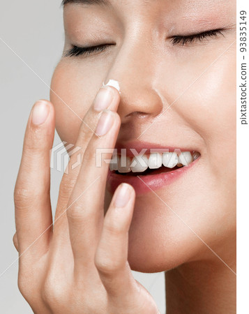 Closeup ardent girl with soft makeup applying moisturizing cream on her nose. 93835149