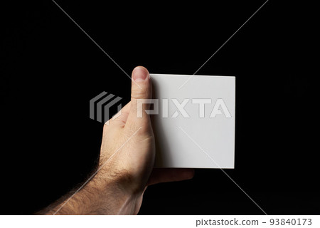 A man's hand holds a small paper white box on a black background. A man's hand holds a small paper white box on a black background. 93840173