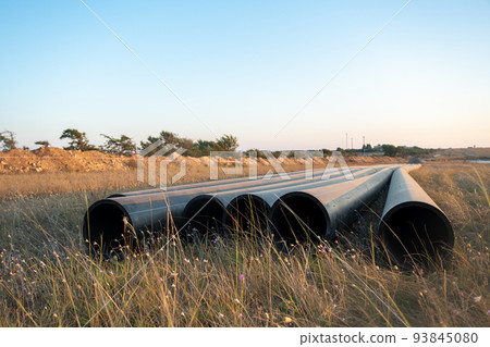 Pipes for laying water pipes lie on the lawn. Sunset, the rays of the sun illuminate the construction site Pipes for laying water pipes lie on the lawn. Sunset, the rays of the sun illuminate the construction site 93845080
