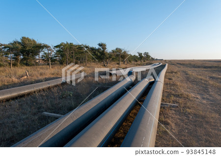 Pipes for laying water pipes lie on the lawn. Sunset, the rays of the sun illuminate the construction site 93845148