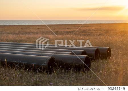 Pipes for laying water pipes lie on the lawn. Sunset, the rays of the sun illuminate the construction site Pipes for laying water pipes lie on the lawn. Sunset, the rays of the sun illuminate the construction site 93845149
