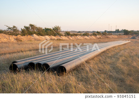Pipes for laying water pipes lie on the lawn. Sunset, the rays of the sun illuminate the construction site 93845151