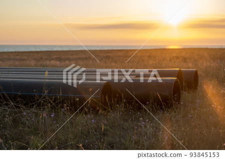 Pipes for laying water pipes lie on the lawn. Sunset, the rays of the sun illuminate the construction site 93845153