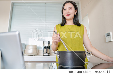 一位年輕女子一邊在平板電腦上觀看視頻一邊做飯 一位年輕女子一邊在平板電腦上觀看視頻一邊做飯 93848211