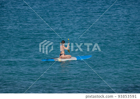 A girl with an oar floats on a board on the sea 93853591