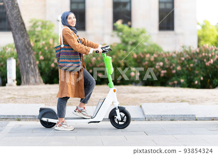Muslim woman posing while using an electric scooter 93854324