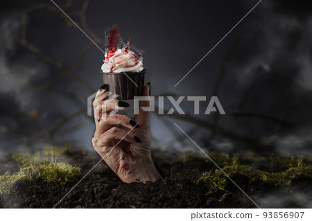 Hand out of grave holding Halloween cupcake. Halloween muffin. Halloween creative food. Hand out of grave holding Halloween cupcake. Halloween muffin. Halloween creative food. 93856907
